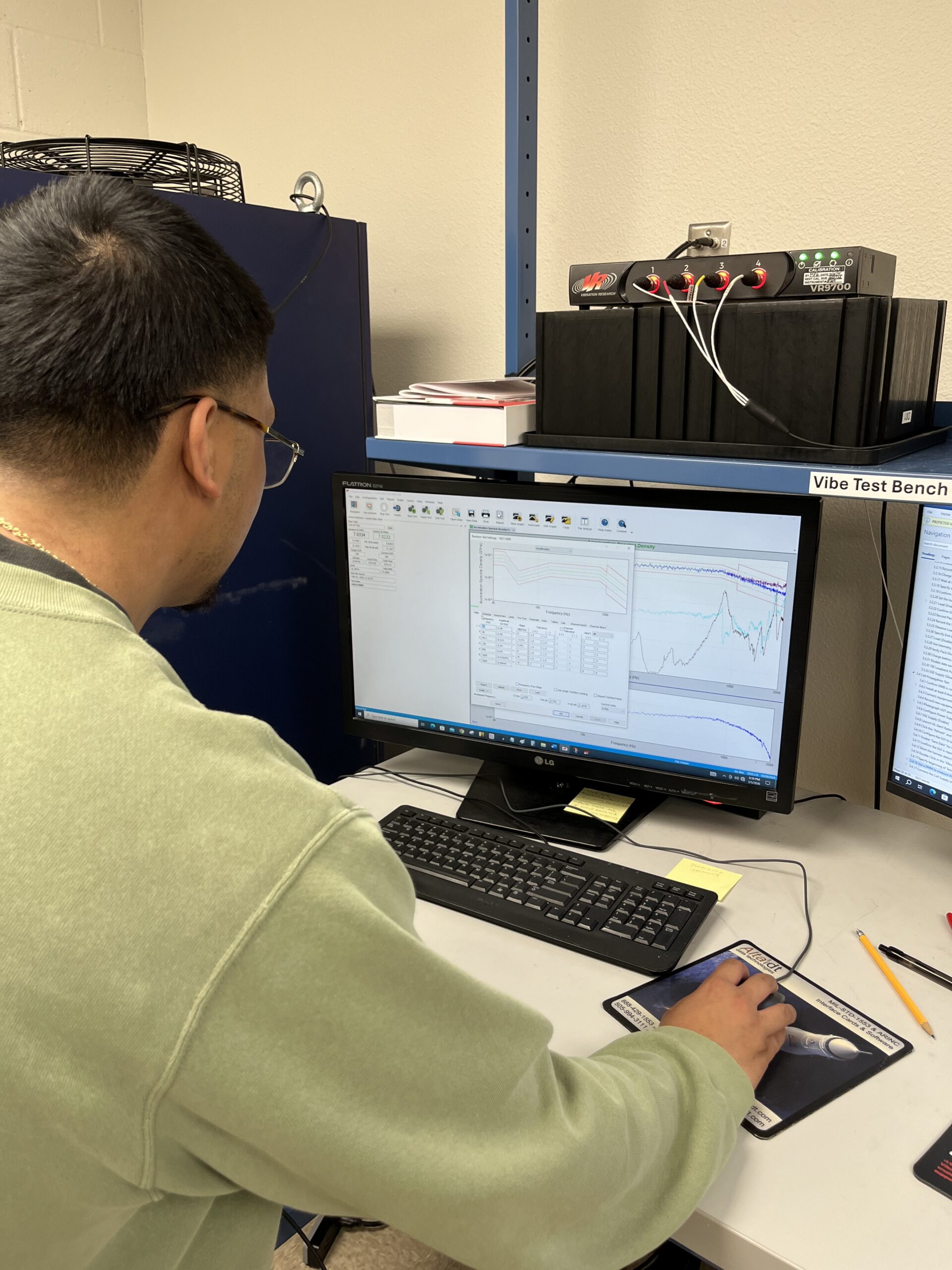 Person analyzing data on a computer screen labeled "Vibe Test Bench" with graphs and spreadsheets displayed